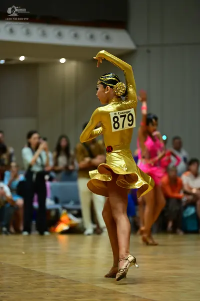 Dancesport competitor #879: Female dancer 1: gold satin long-sleeved latin dress with a flared skirt and a g