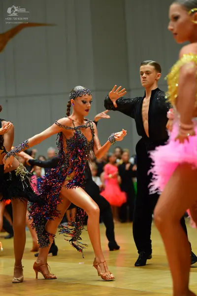 Dancesport competitor: Female dancer in center: dark Latin dress with colorful sequins (blue, purple, p