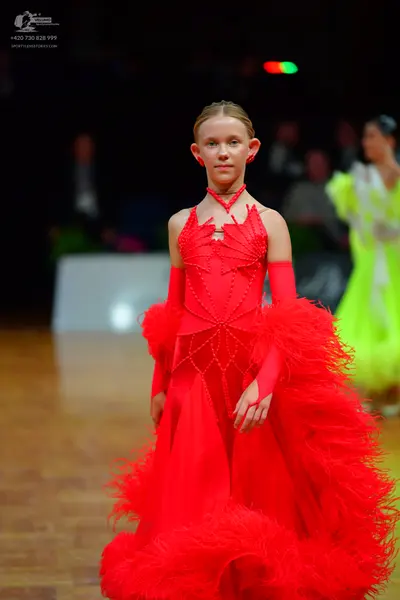 Dancesport competitor: Female dancer in foreground: red ballroom dress with a voluminous, textured, fea