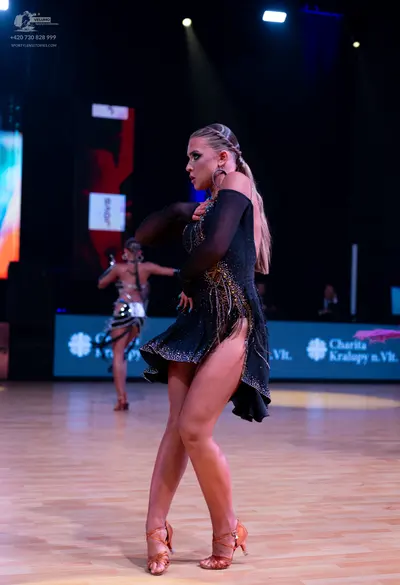 Dancesport competitor: Female dancer (foreground): black Latin dress with long sheer sleeves and gold/b