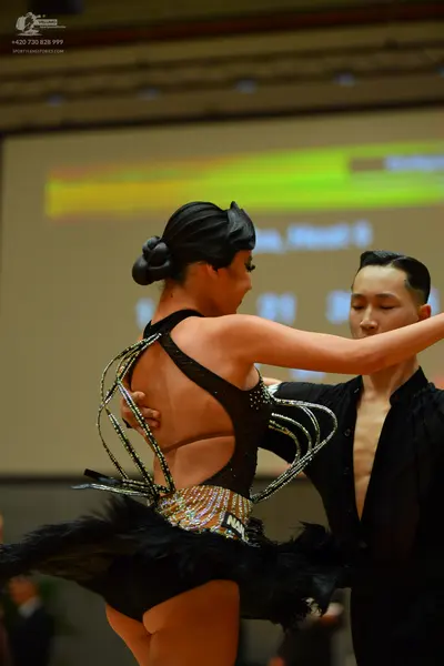 Dancesport competitor: Female dancer: black Latin dance costume featuring thin, decorative, crisscrossi