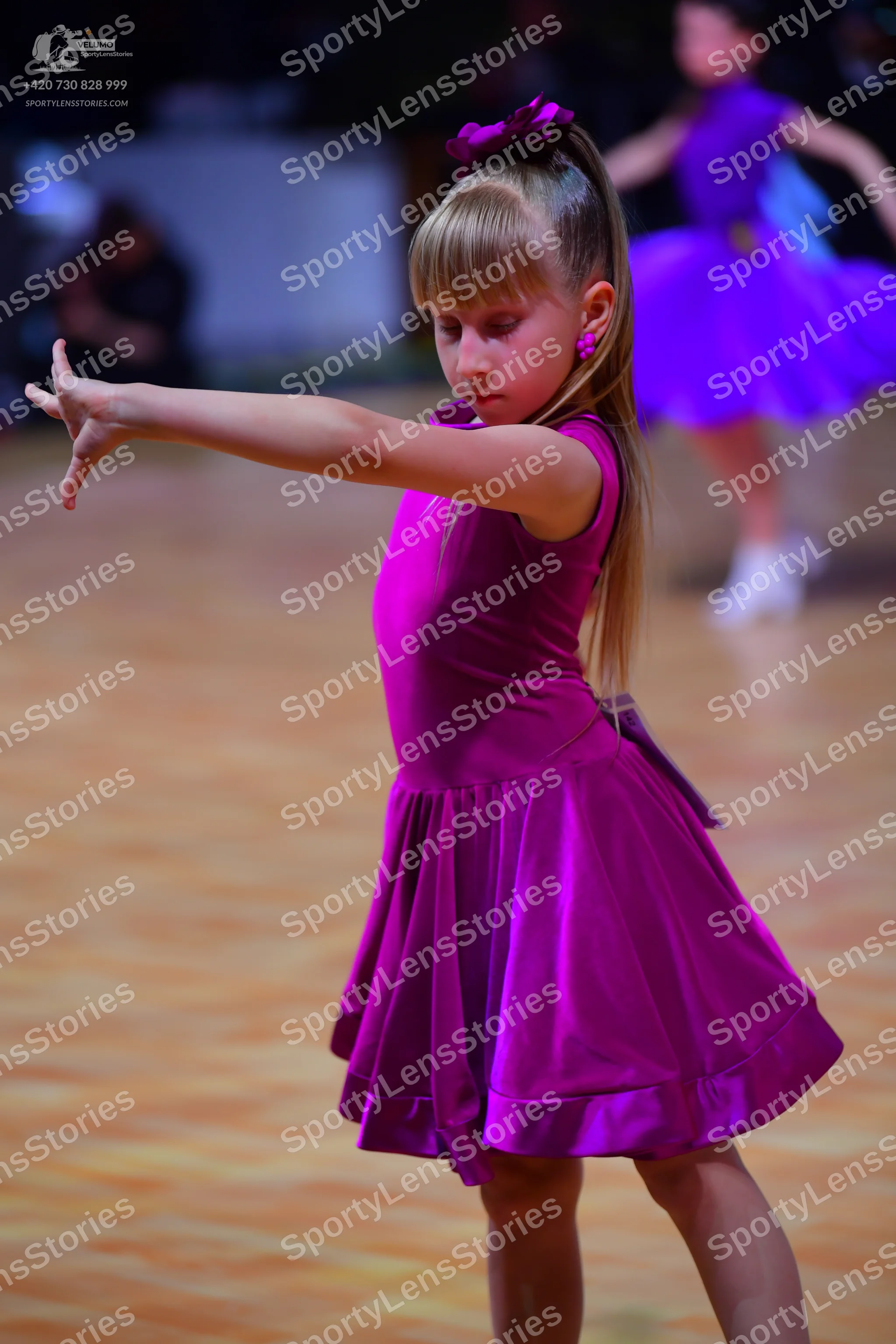 Dancesport competitor: Foreground dancer: purple sleeveless satin-like dress with a flared skirt and a