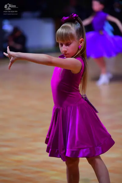 Dancesport competitor: Foreground dancer: purple sleeveless satin-like dress with a flared skirt and a 