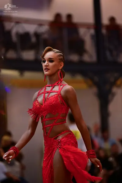 Dancesport competitor: Female dancer: red latin dress with sequins, cutouts, and fringe, and matching r