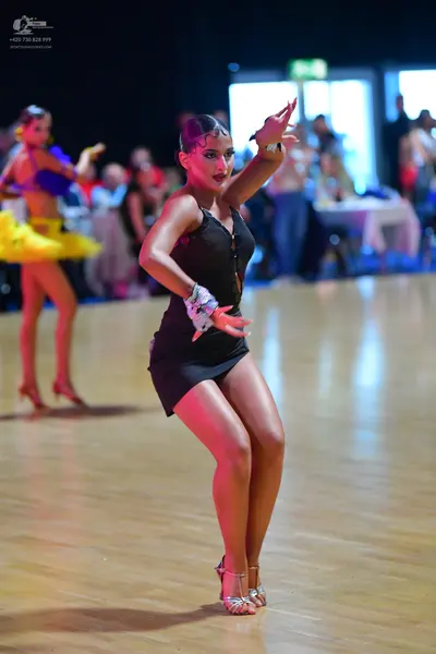 Dancesport competitor: Female dancer in foreground: black sleeveless Latin dress and silver strappy dan
