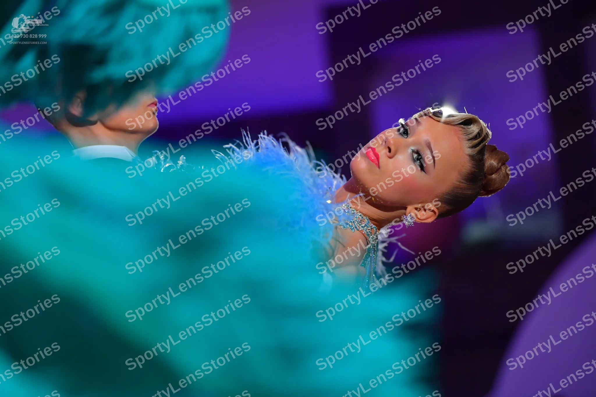 Dancesport competitor: Female dancer: light blue/teal costume with feathers around the neck and sparkly