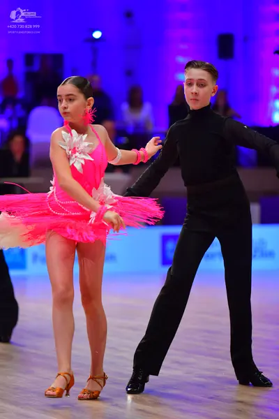 Dancesport competitor: Female dancer: bright pink Latin dance dress with white floral embellishments an