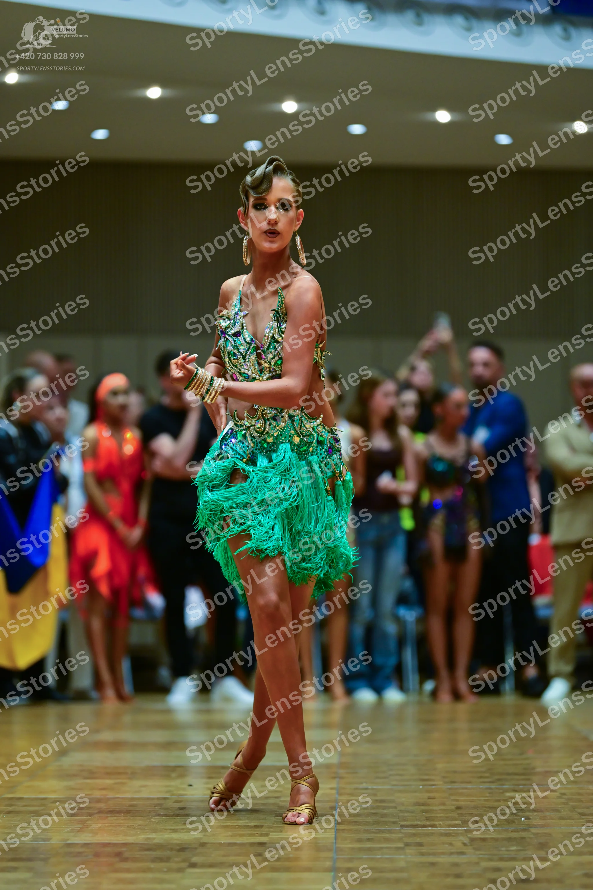 Dancesport competitor: Female dancer in foreground: green latin dress with fringe and blue, silver, and
