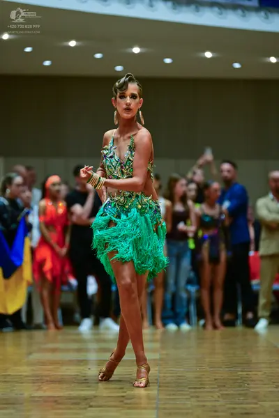 Dancesport competitor: Female dancer in foreground: green latin dress with fringe and blue, silver, and