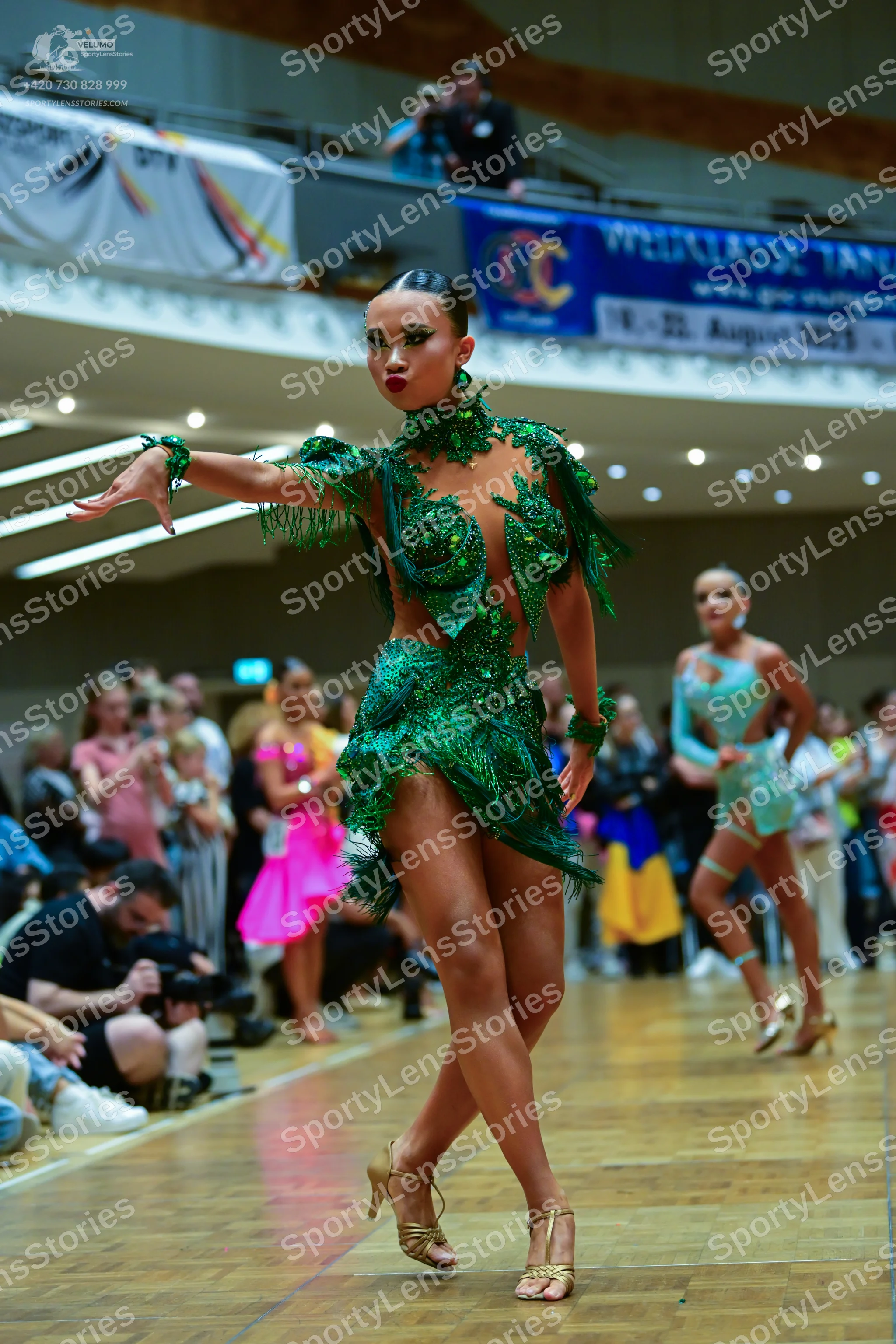 Dancesport competitor: Female dancer in foreground: emerald green latin dress with intricate sequin lac
