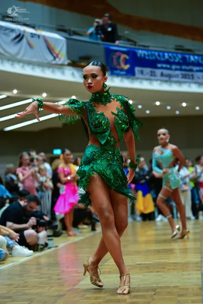 Dancesport competitor: Female dancer in foreground: emerald green latin dress with intricate sequin lac