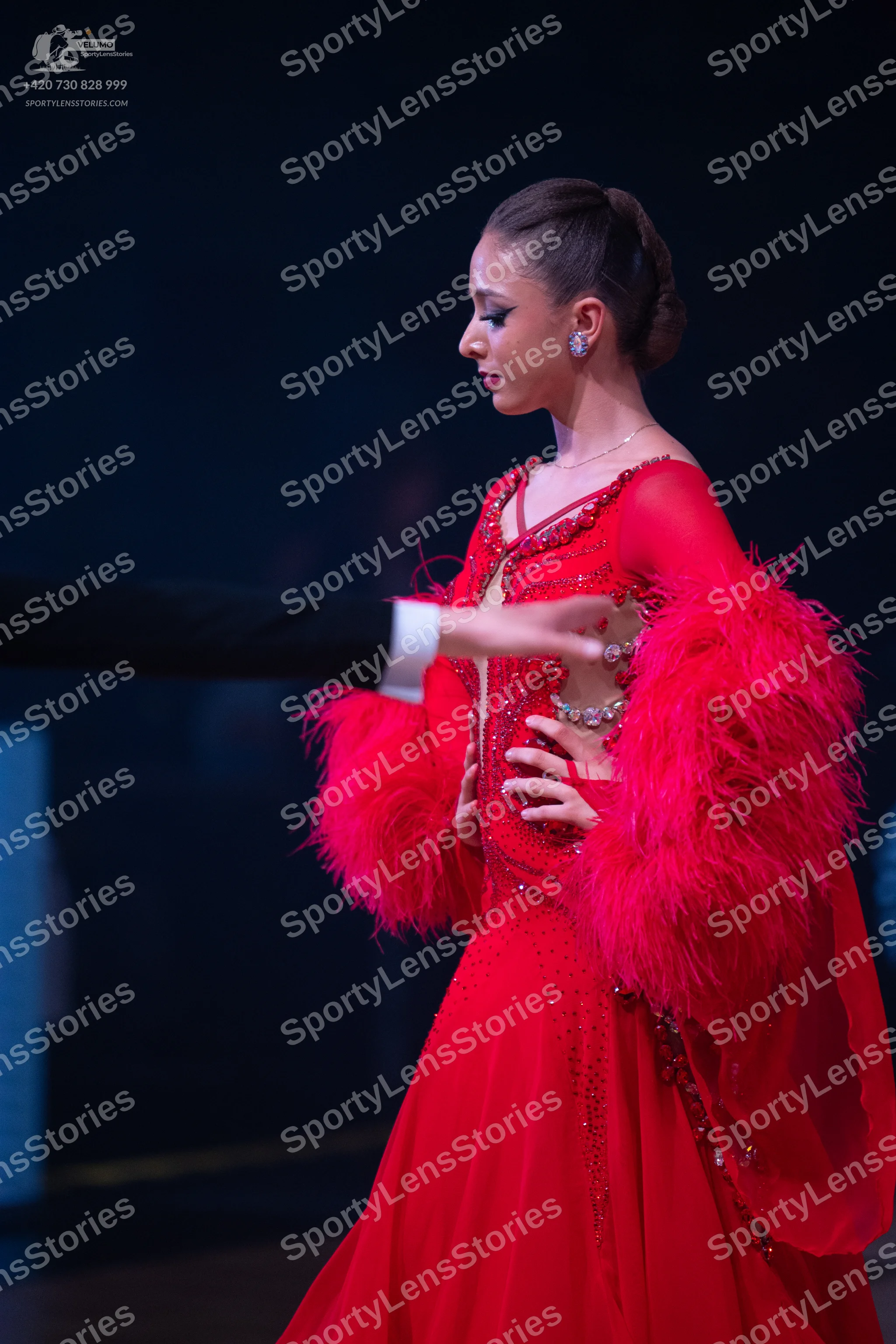 Dancesport competitor: Female dancer: red ballroom gown with feather-trimmed sleeves and crystal embell