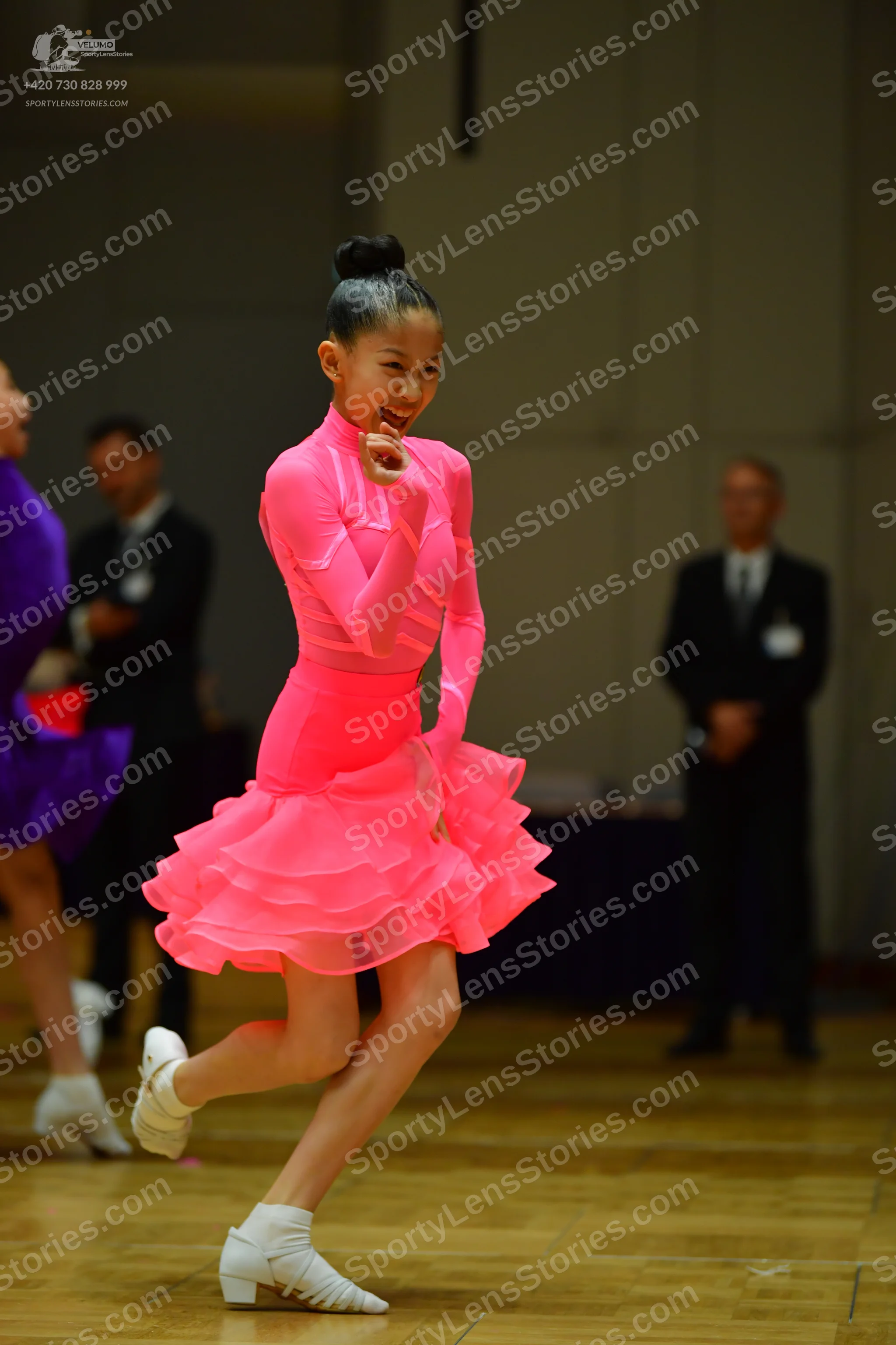 Dancesport competitor: Female dancer in foreground: bright pink, long-sleeved latin dress with a tiered