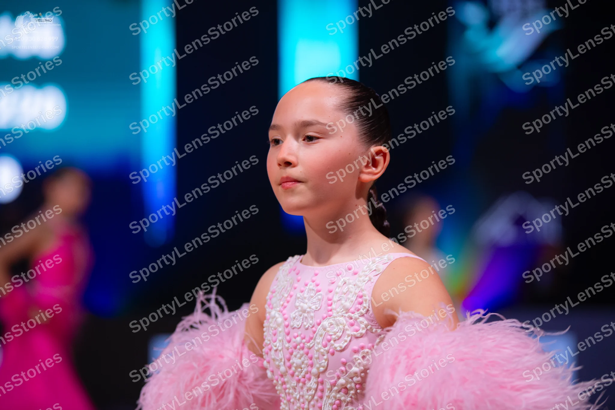 Dancesport competitor: Female dancer in foreground: light pink sleeveless dress with a white sequined f