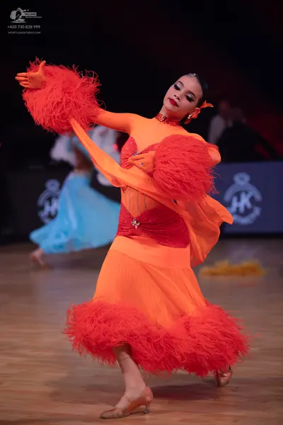 Dancesport competitor: Female dancer in foreground: orange latin dress with large red feather trim on t
