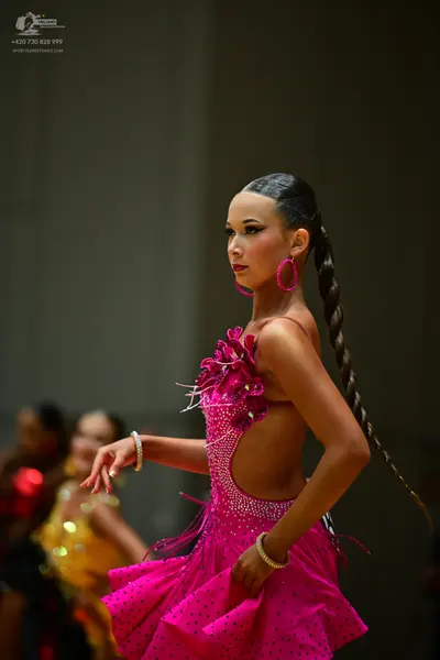Dancesport competitor: Female dancer in foreground: bright pink Latin dance dress with dark patterns or