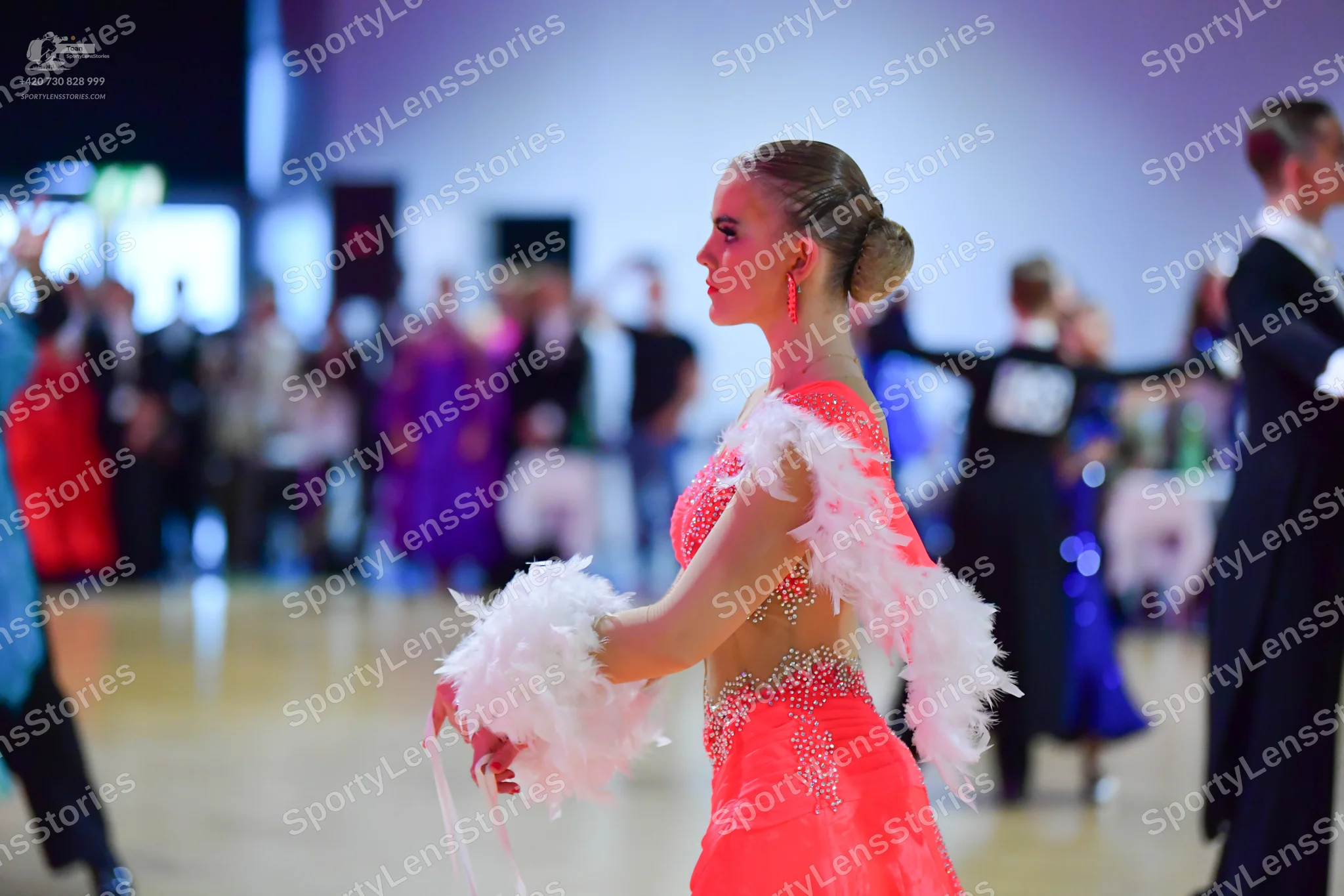 Dancesport competitor: Female dancer in foreground: coral pink Latin dress with white fluffy/feathered