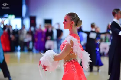 Dancesport competitor: Female dancer in foreground: coral pink Latin dress with white fluffy/feathered 