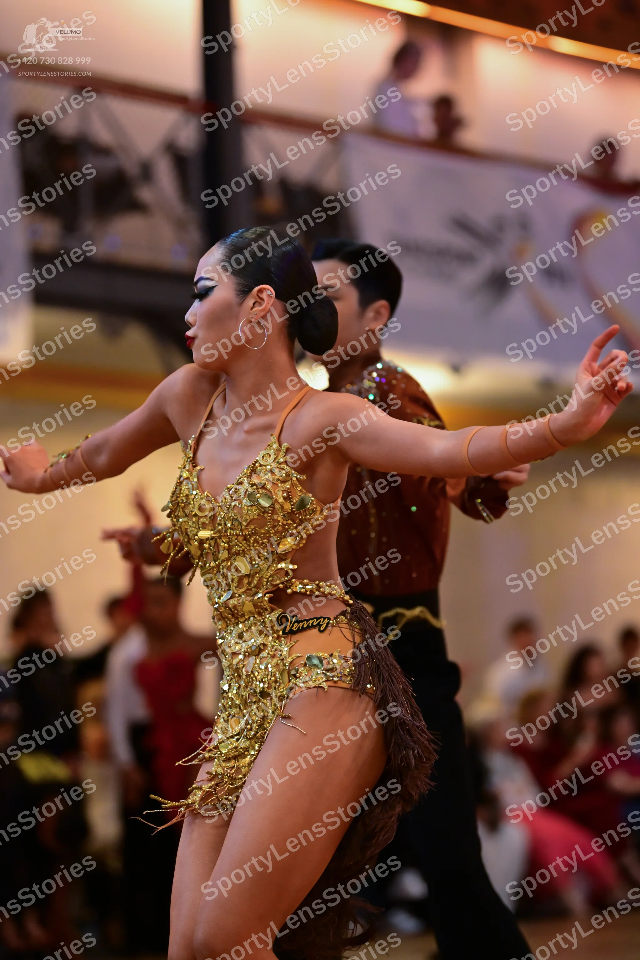 Dancesport competitor: Female dancer: gold/champagne-colored Latin dance bodysuit heavily embellished w