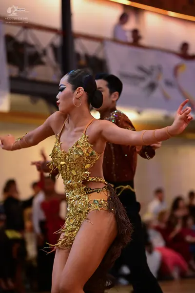 Dancesport competitor: Female dancer: gold/champagne-colored Latin dance bodysuit heavily embellished w