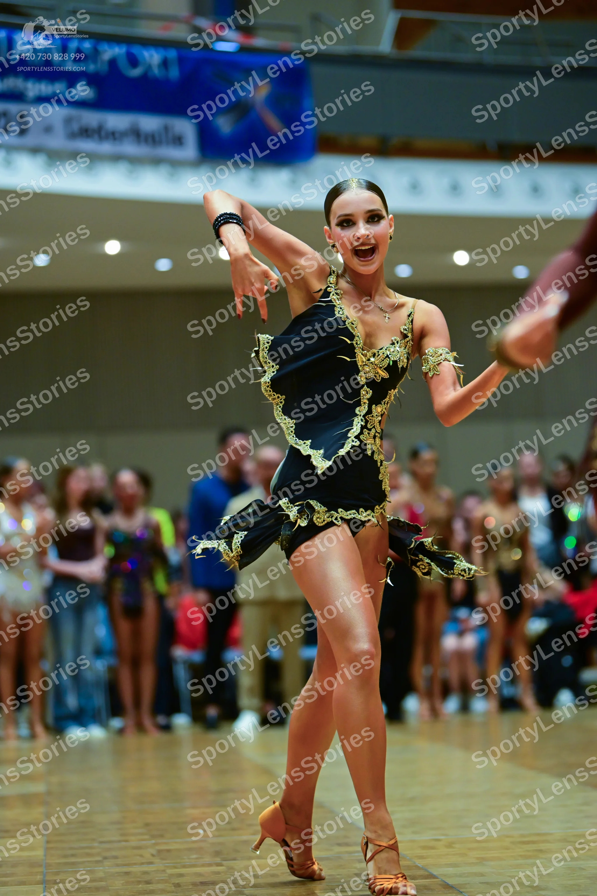 Dancesport competitor: Main female dancer: black latin dress with gold trim and an asymmetrical hem, ac