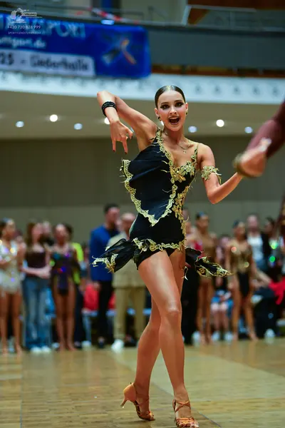 Dancesport competitor: Main female dancer: black latin dress with gold trim and an asymmetrical hem, ac