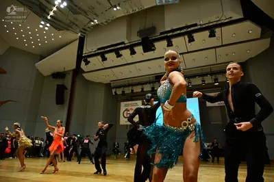 Dancesport competitor: Foreground female dancer: teal/turquoise sequined Latin dance costume with a seq