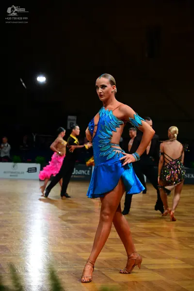 Dancesport competitor: Female dancer in foreground: blue latin dress with light blue/teal scale-like or