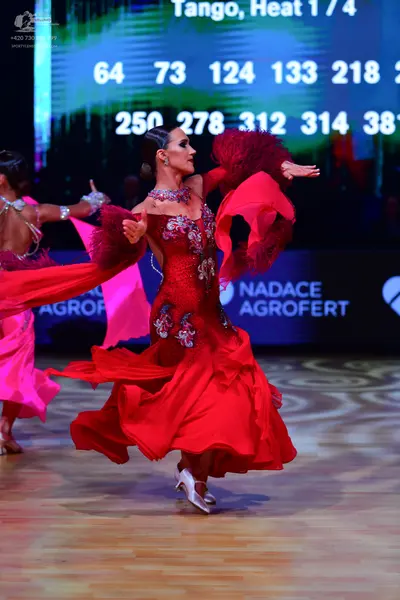 Dancesport competitor: Female dancer in foreground: red ballroom dress with a sequined bodice and large
