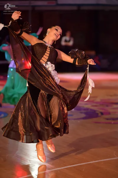 Dancesport competitor: Female dancer in foreground: dark brown/bronze ballroom dress with a large, volu