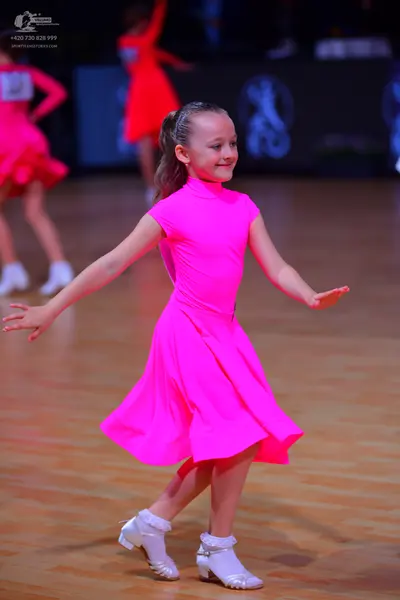 Dancesport competitor: Female dancer in foreground: bright pink short-sleeved latin dress with white da
