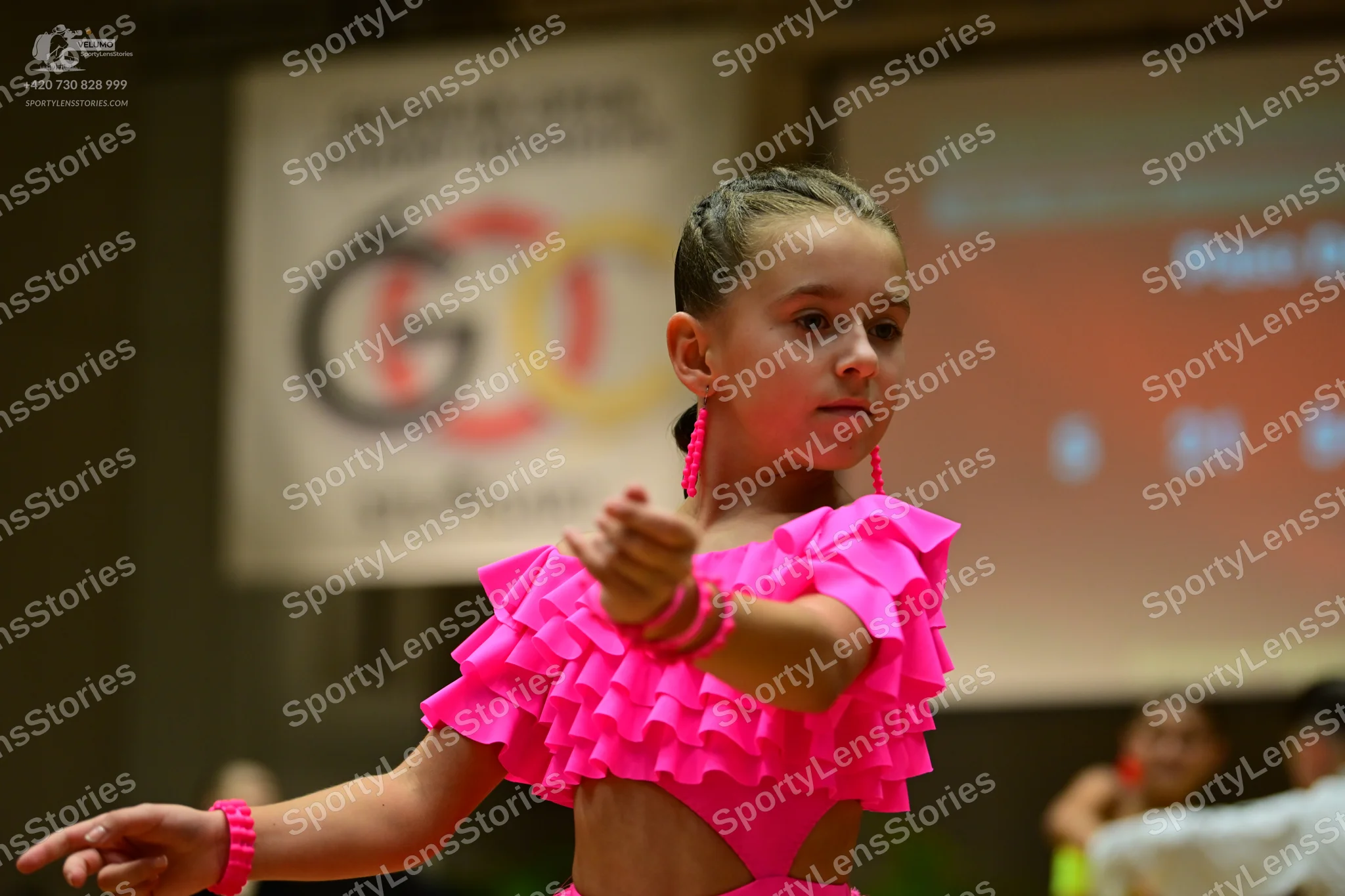 Dancesport competitor: Female dancer: bright pink latin dance costume with ruffled sleeves and a cutout