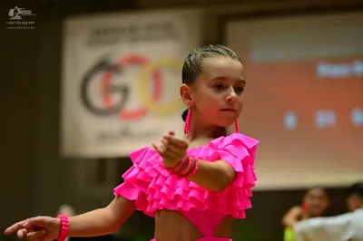 Dancesport competitor: Female dancer: bright pink latin dance costume with ruffled sleeves and a cutout