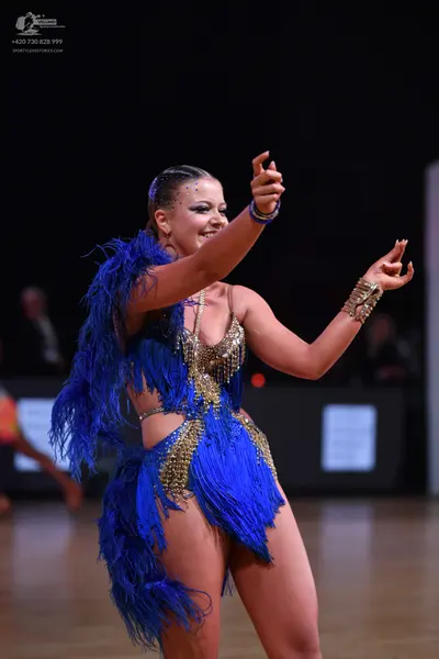 Dancesport competitor: Female dancer: blue Latin dance costume with heavy blue fringe, gold sequins, an