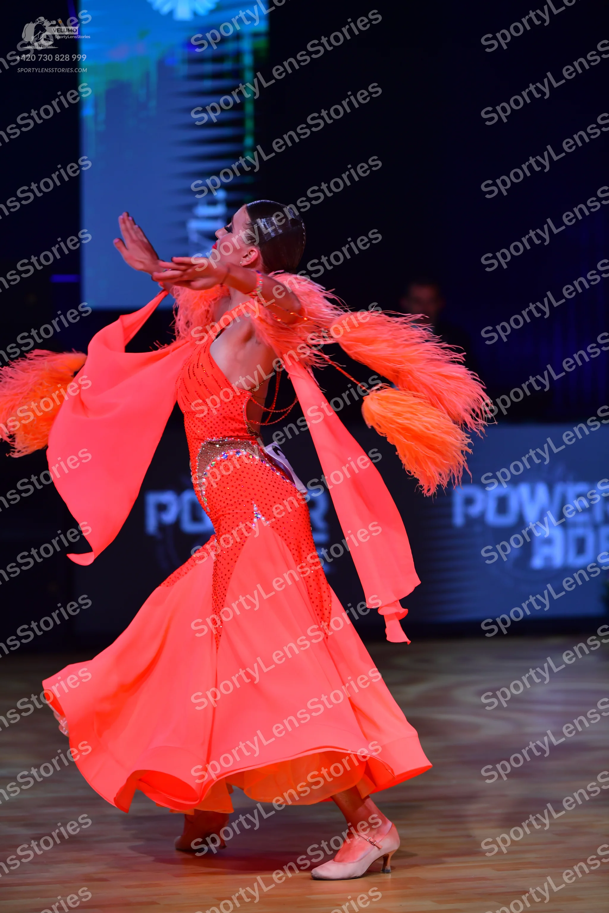 Dancesport competitor: Female dancer: bright orange Latin dress with large, feathery orange fringe on t