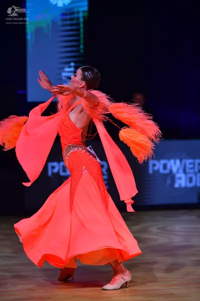 Dancesport competitor: Female dancer: bright orange Latin dress with large, feathery orange fringe on t