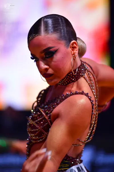 Dancesport competitor: Female dancer: dark burgundy Latin costume heavily embellished with sequins and 