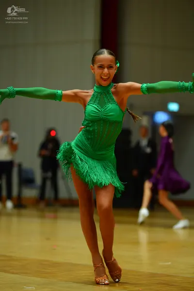 Dancesport competitor: Female dancer in foreground: green latin dress with fringe and long matching arm