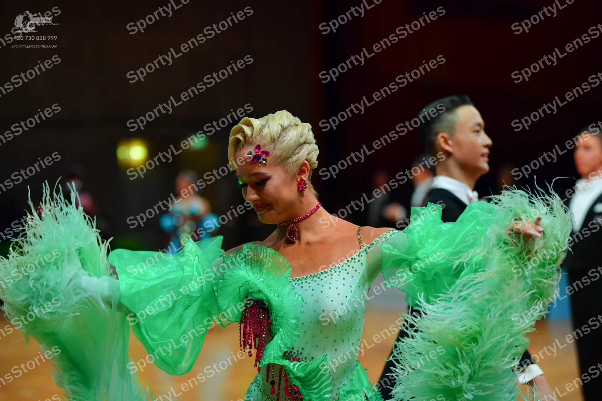 Dancesport competitor: Female dancer: light green Latin dress with heavy fringe, sequins, and a pink fl