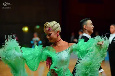 Dancesport competitor: Female dancer: light green Latin dress with heavy fringe, sequins, and a pink fl