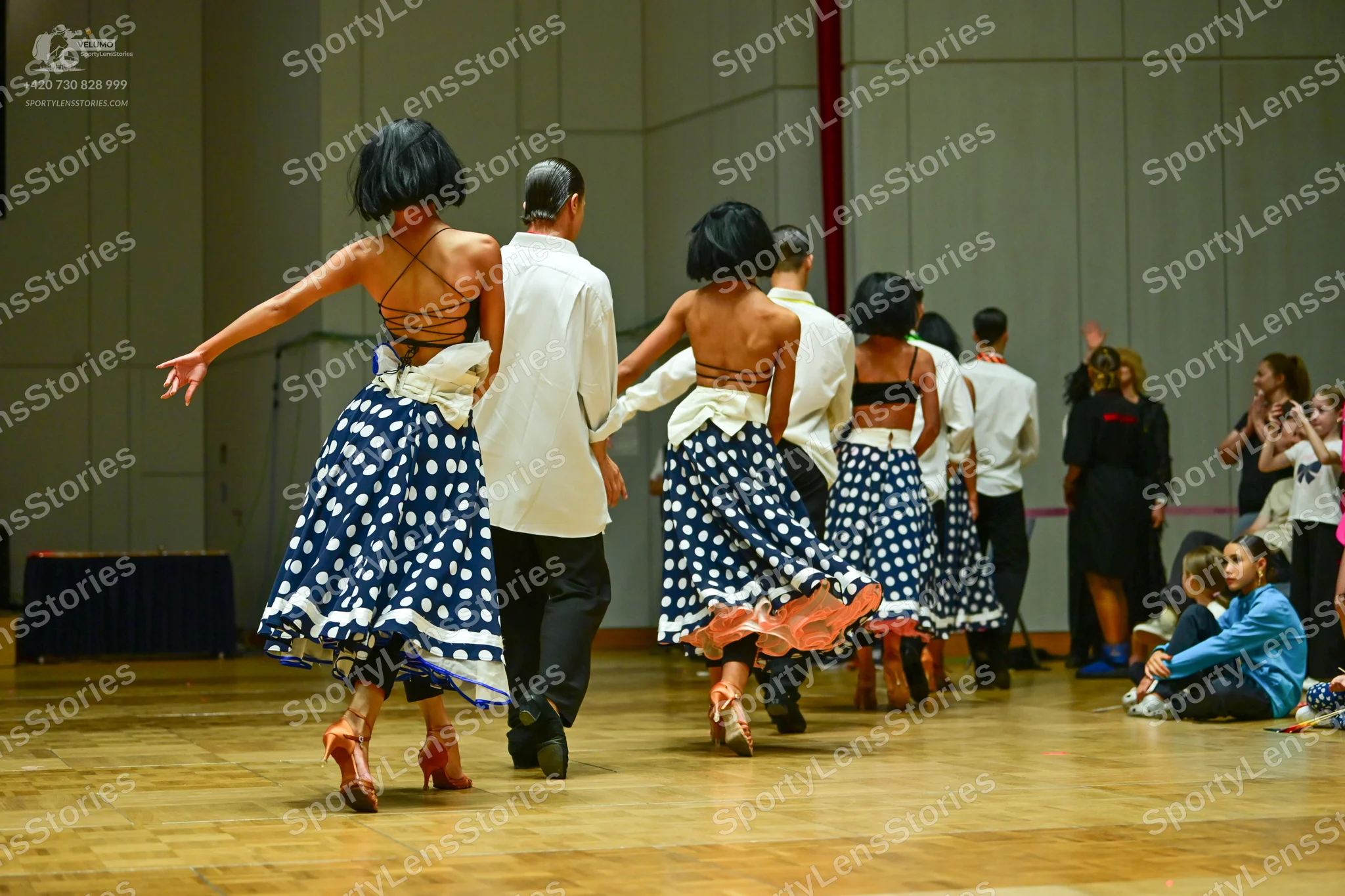 Dancesport competitor: Three female dancers: blue and white polka dot skirts, black strappy tops, and b