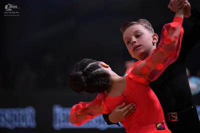Dancesport competitor: Male dancer: black long-sleeved top with a black waistband featuring a red/pink 