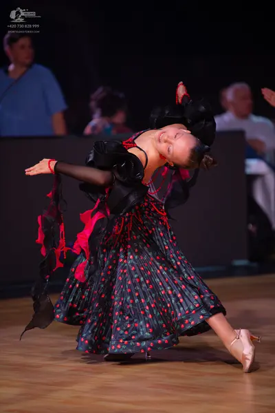 Dancesport competitor: Female dancer: dramatic black and red dance dress with large ruffled shoulder pi