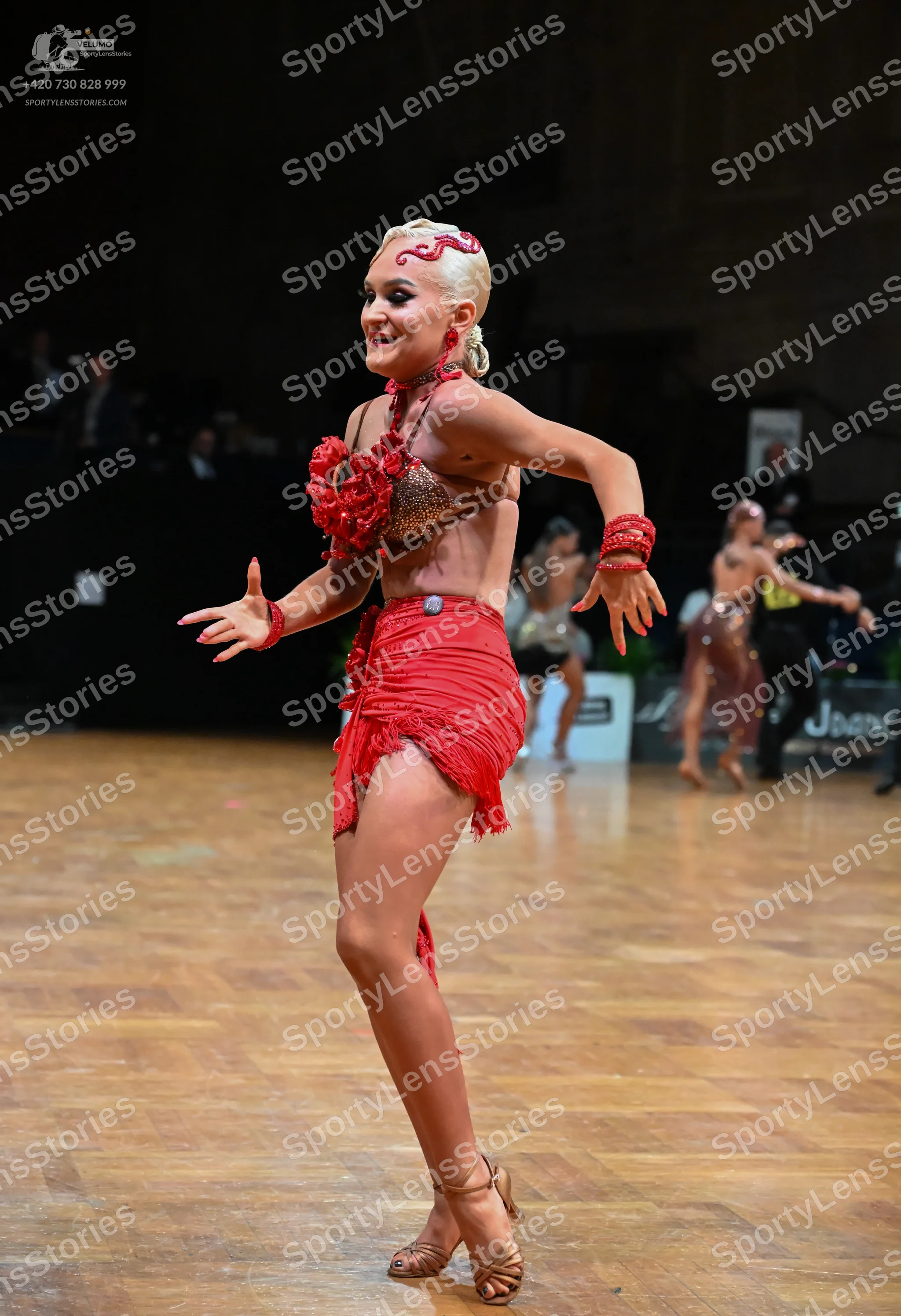 Dancesport competitor: Female dancer in foreground: red latin dress with a decorated bodice and a fring