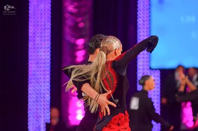 Dancesport competitor: Female dancer: black long-sleeved Latin dress with red lace or floral embellishm