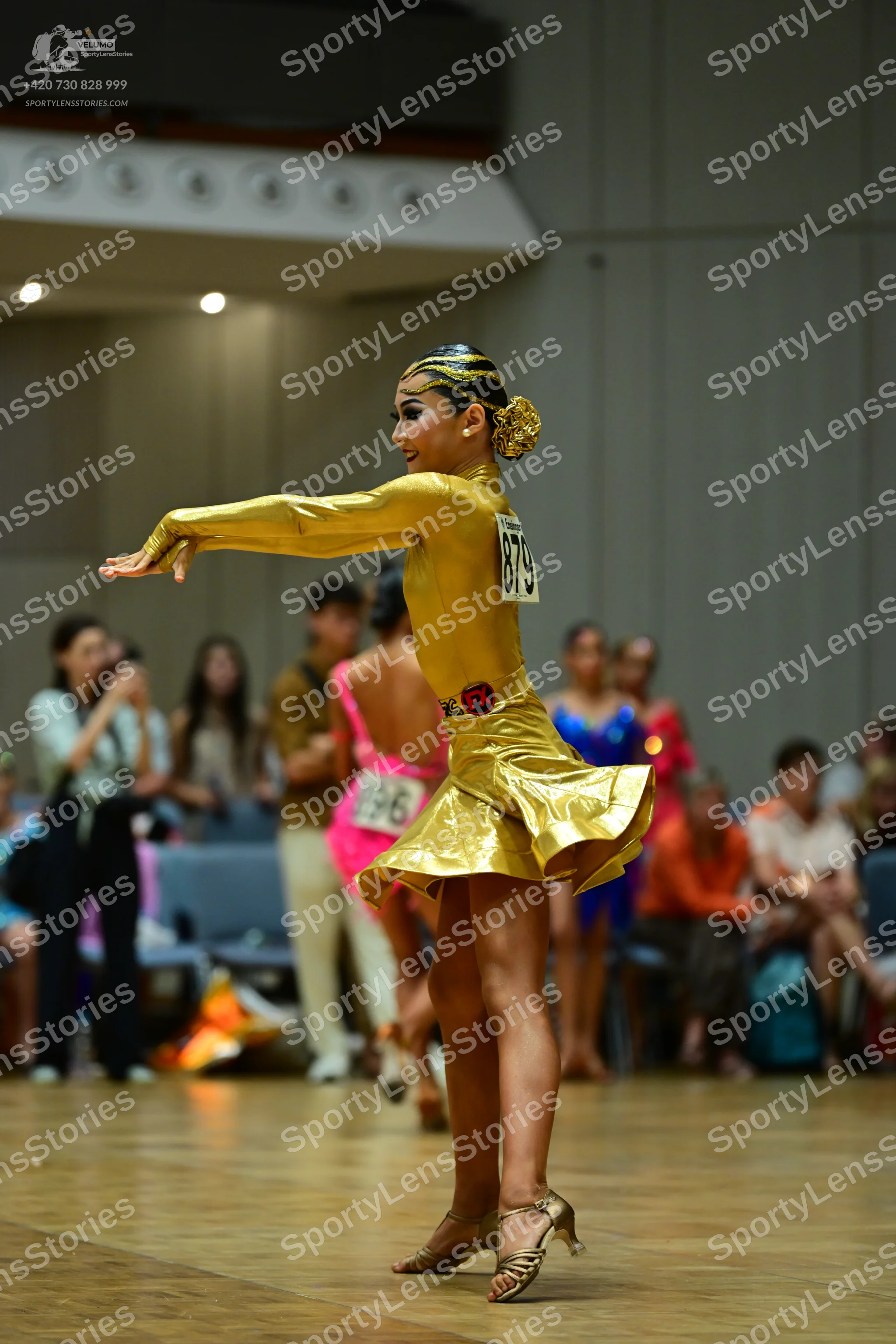 Dancesport competitor #879: Female dancer: gold metallic long-sleeved latin dress with a flared skirt, gold