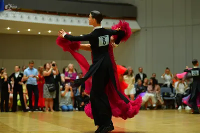 Dancesport competitor: Male dancer: black long-sleeved top with a white collar and black trousers, feat