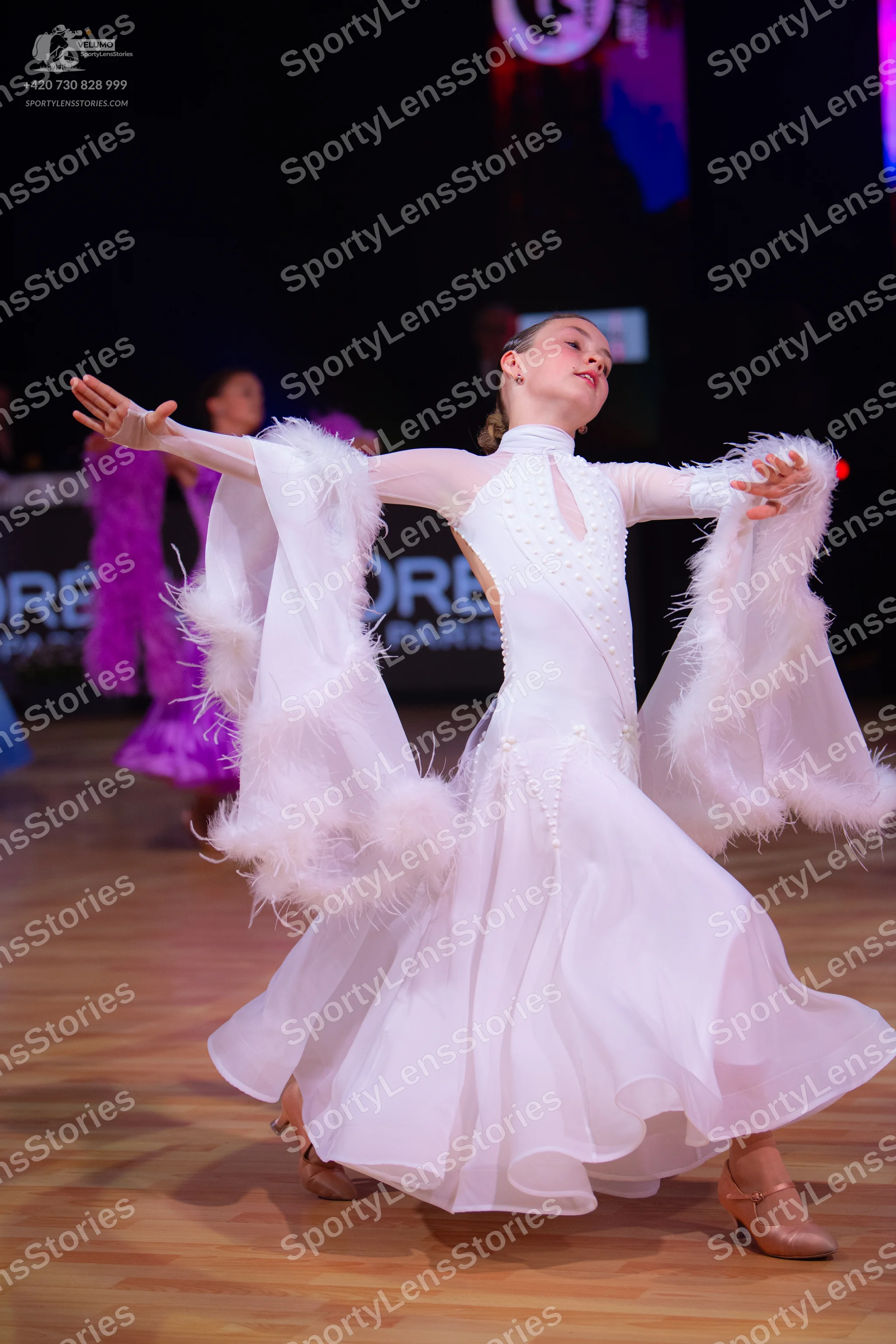Dancesport competitor: Female dancer in foreground: white long-sleeved ballroom dress with large feathe