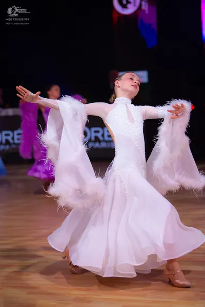 Dancesport competitor: Female dancer in foreground: white long-sleeved ballroom dress with large feathe