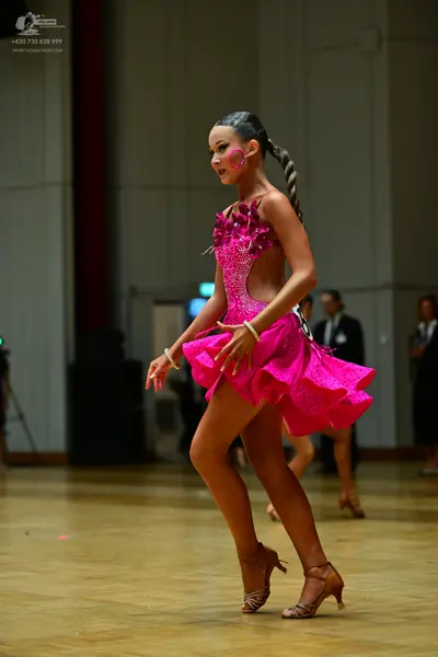 Dancesport competitor: Female dancer: bright pink sequined latin dress with cut-out details and a short